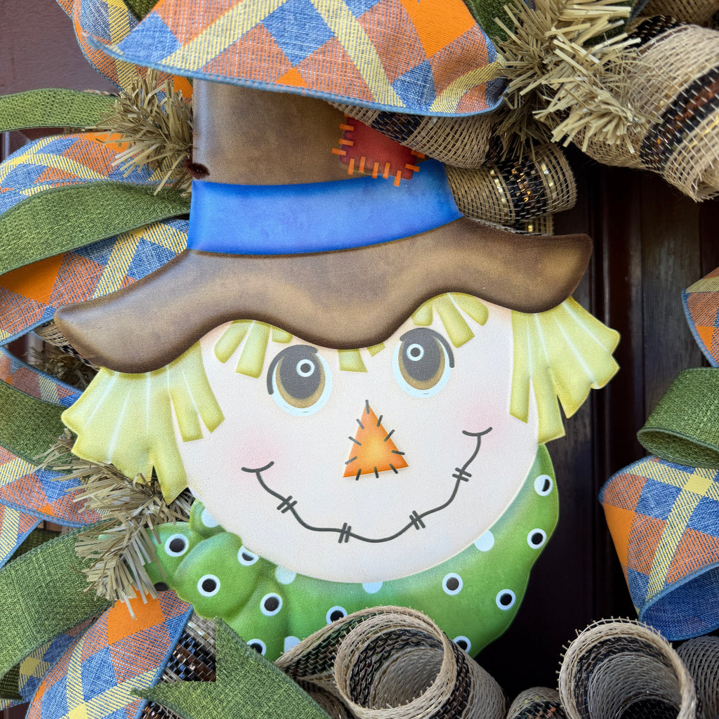 colorful scarecrow fall wreath. With its smiling scarecrow, warm autumn tones, and playful plaid ribbon, this wreath feels lighthearted, friendly, and full of seasonal charm.
