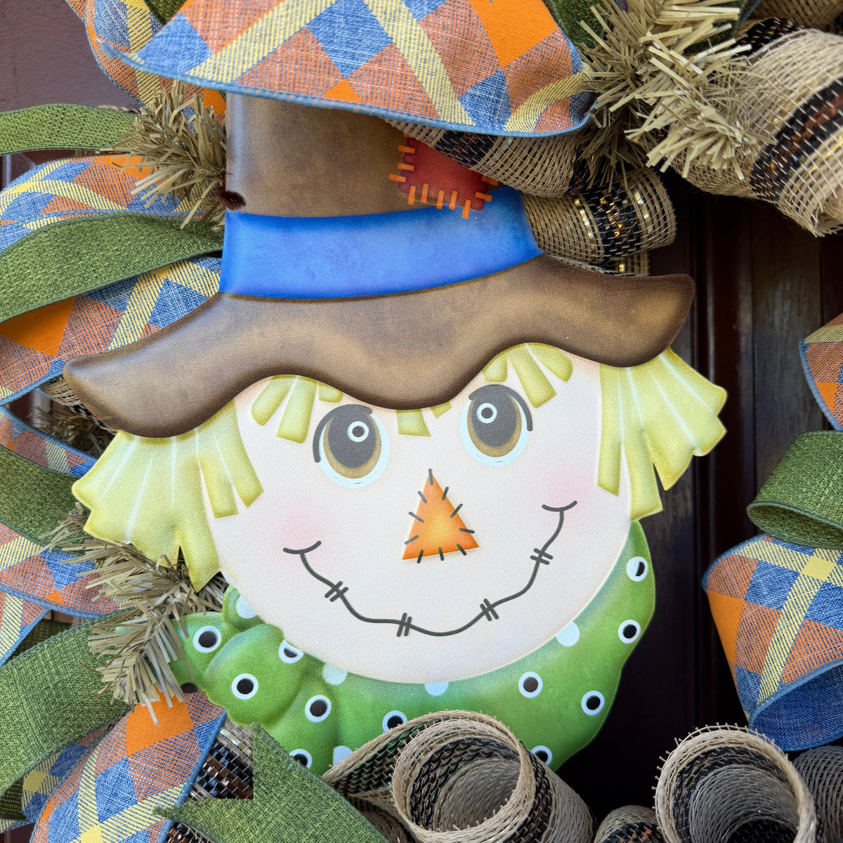 colorful scarecrow fall wreath. With its smiling scarecrow, warm autumn tones, and playful plaid ribbon, this wreath feels lighthearted, friendly, and full of seasonal charm.
