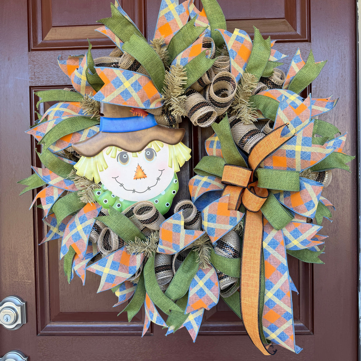 colorful scarecrow fall wreath. With its smiling scarecrow, warm autumn tones, and playful plaid ribbon, this wreath feels lighthearted, friendly, and full of seasonal charm.