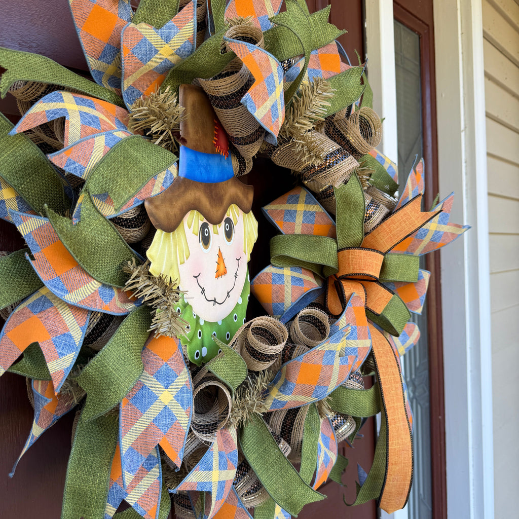 colorful scarecrow fall wreath. With its smiling scarecrow, warm autumn tones, and playful plaid ribbon, this wreath feels lighthearted, friendly, and full of seasonal charm.
