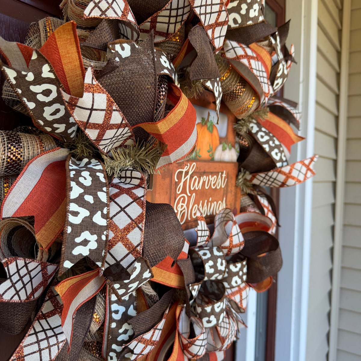 Harvest Blessings wreath. Rich pumpkin orange, deep brown, cream, and soft green come together in a full, layered design that feels cozy, cheerful, and perfect for the season.