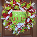 A festive Christmas wreath made of red, green, and white mesh ribbons with candy cane, holly, and snowflake patterns, featuring a central square sign that reads 'holly JOLLY' in white and red lettering.