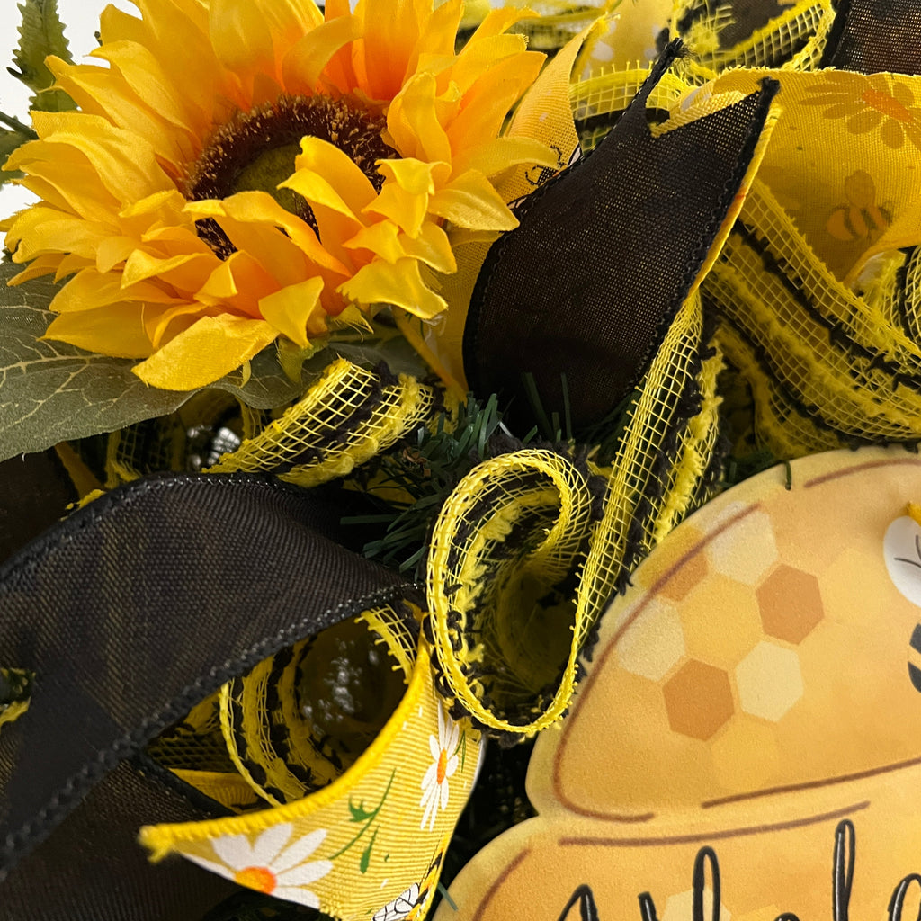 Handmade bee and sunflower wreath featuring a Welcome to Our Hive sign, yellow and black ribbons, daisy accents, and bright sunflowers for summer front door decor.