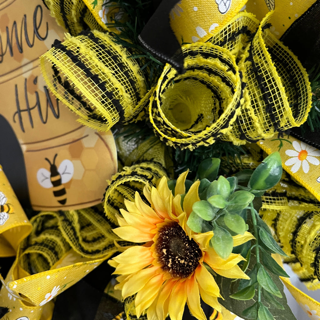 Handmade bee and sunflower wreath featuring a Welcome to Our Hive sign, yellow and black ribbons, daisy accents, and bright sunflowers for summer front door decor.