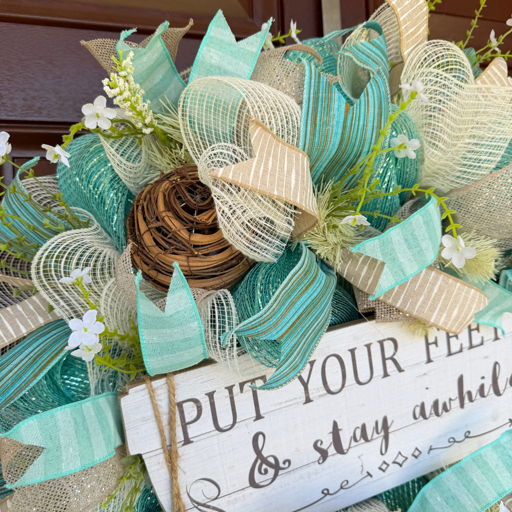 Handmade coastal welcome wreath with aqua blue, cream, and beige ribbons, floral accents, and a farmhouse-style welcome sign for beach house or summer front door decor.