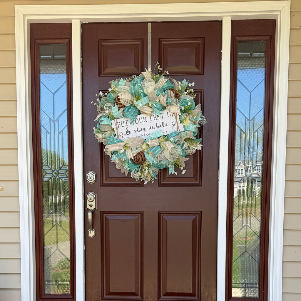 Handmade coastal welcome wreath with aqua blue, cream, and beige ribbons, floral accents, and a farmhouse-style welcome sign for beach house or summer front door decor.