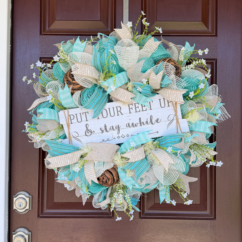 Handmade coastal welcome wreath with aqua blue, cream, and beige ribbons, floral accents, and a farmhouse-style welcome sign for beach house or summer front door decor.