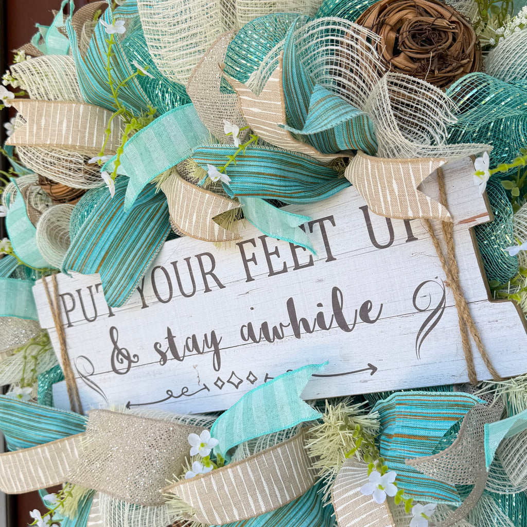Handmade coastal welcome wreath with aqua blue, cream, and beige ribbons, floral accents, and a farmhouse-style welcome sign for beach house or summer front door decor.