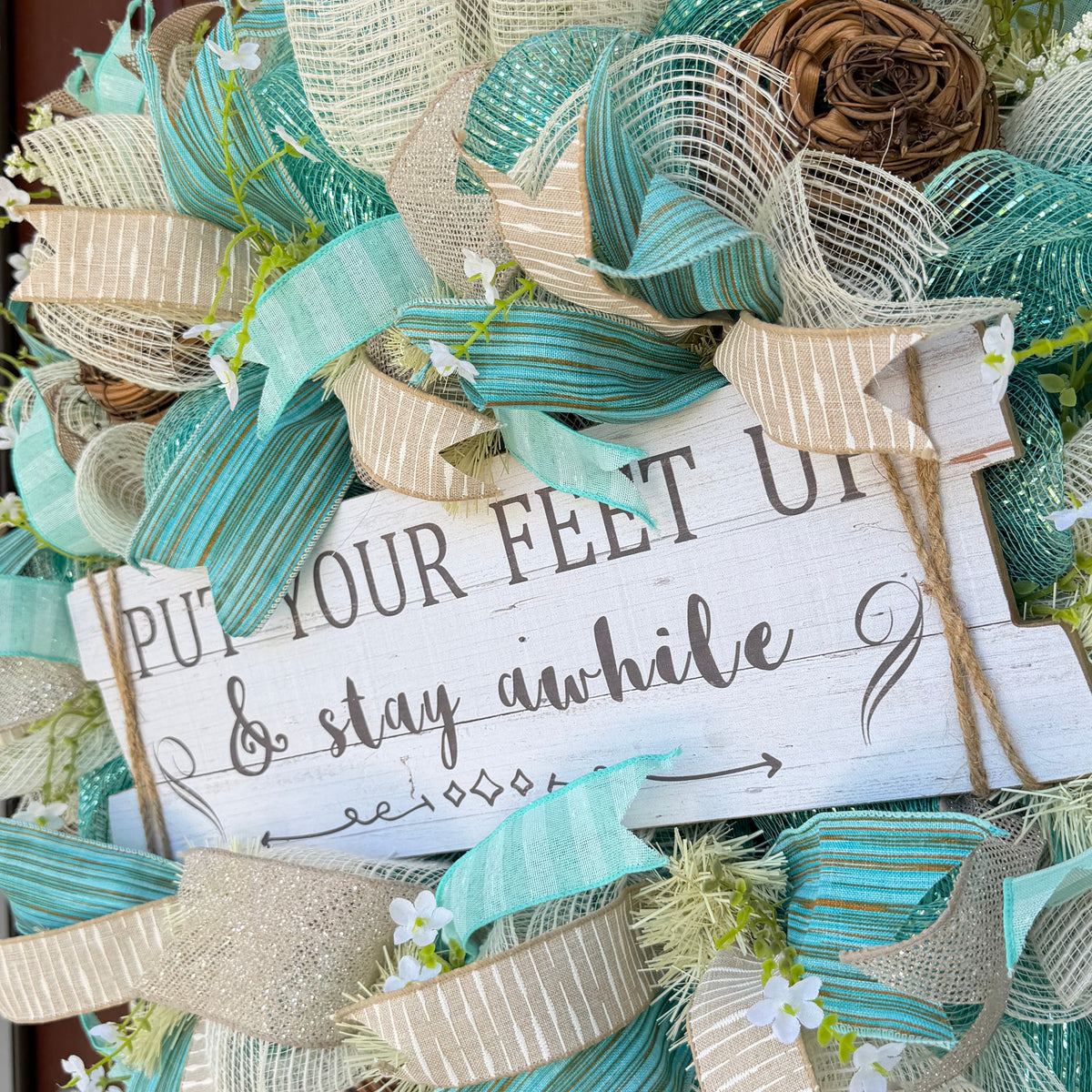 Handmade coastal welcome wreath with aqua blue, cream, and beige ribbons, floral accents, and a farmhouse-style welcome sign for beach house or summer front door decor.