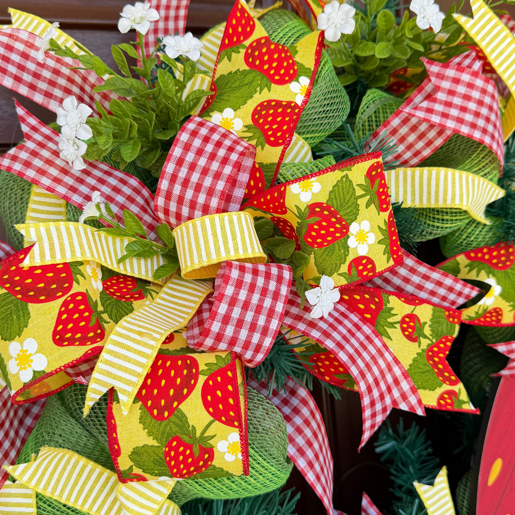 Handmade strawberry summer wreath featuring red gingham ribbons, strawberry print accents, greenery, and a large strawberry centerpiece hanging on a front door.