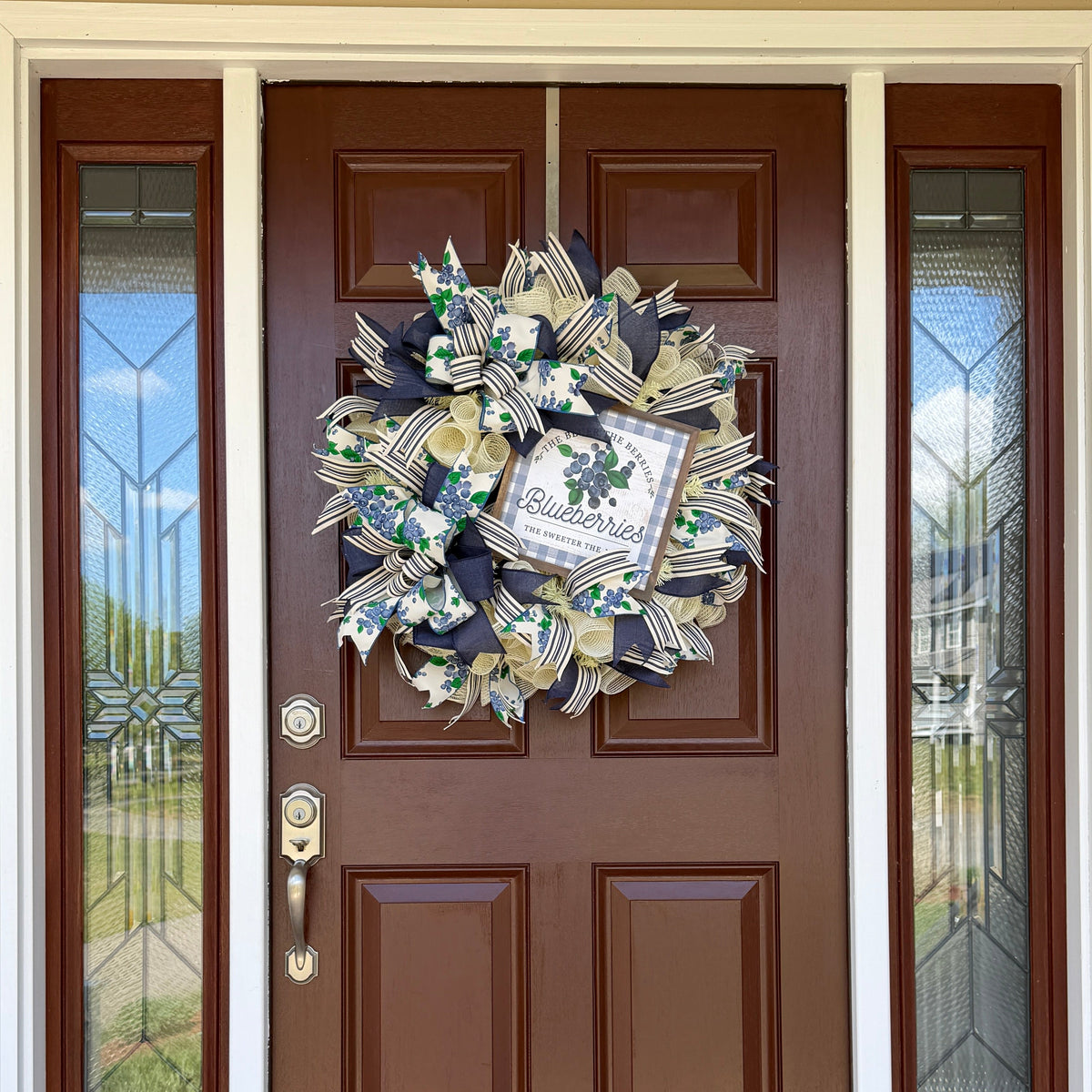 Handmade blueberry farmhouse wreath with navy blue and cream ribbons, blueberry print accents, and a blueberry sign displayed on a front door for summer decorating.