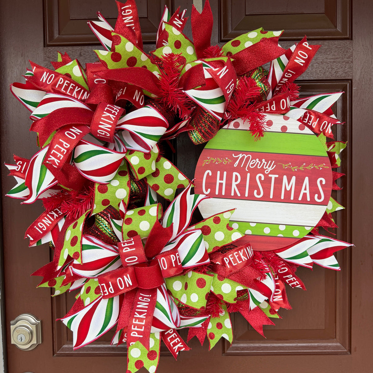 Handmade red and lime green Christmas deco mesh wreath with striped ribbons, No Peeking accents, and Merry Christmas sign.