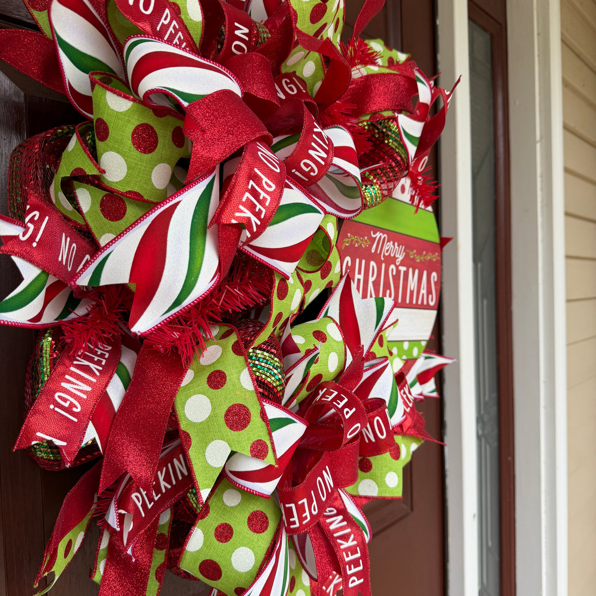 Handmade red and lime green Christmas deco mesh wreath with striped ribbons, No Peeking accents, and Merry Christmas sign.