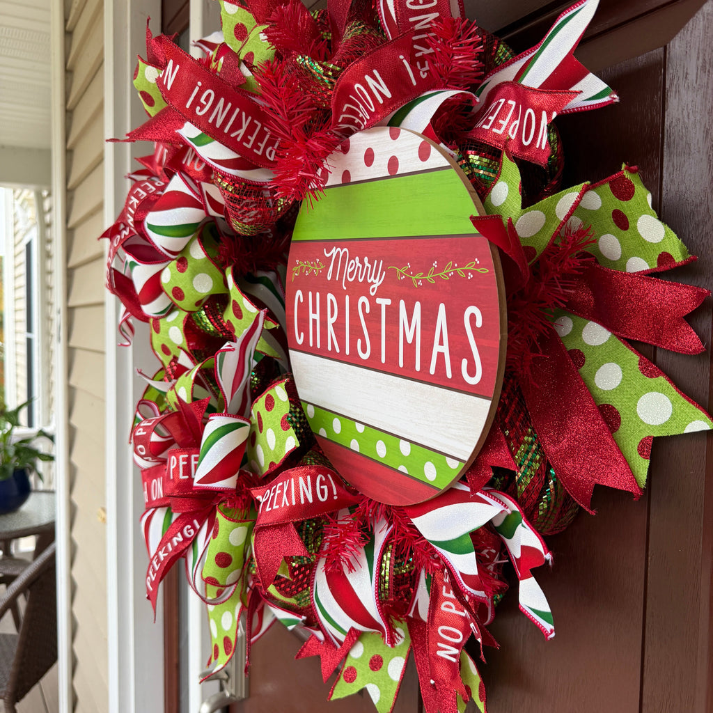 Handmade red and lime green Christmas deco mesh wreath with striped ribbons, No Peeking accents, and Merry Christmas sign.