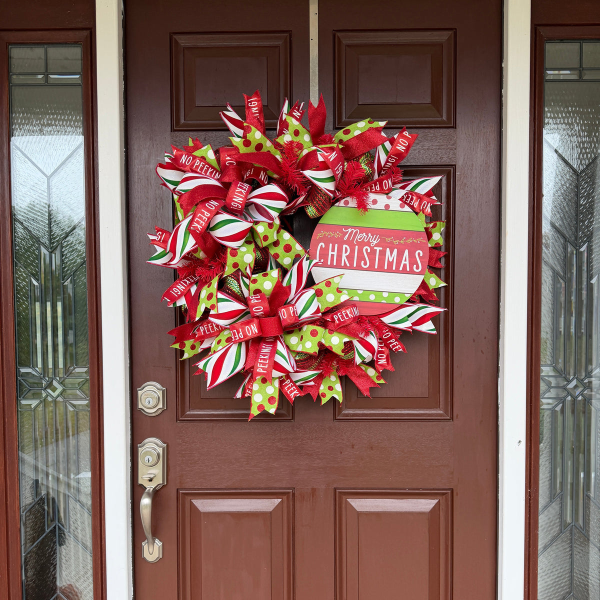 Handmade red and lime green Christmas deco mesh wreath with striped ribbons, No Peeking accents, and Merry Christmas sign.