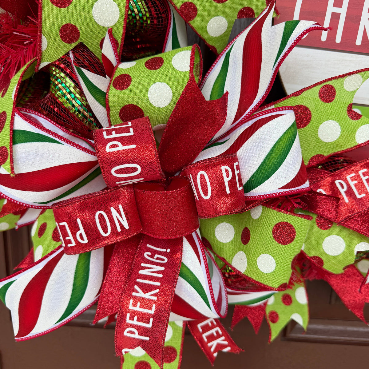 Handmade red and lime green Christmas deco mesh wreath with striped ribbons, No Peeking accents, and Merry Christmas sign.