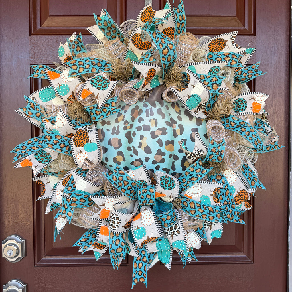 teal leopard-print pumpkin wreath, surrounded by layers of natural-toned deco mesh and coordinating wired ribbons. Pumpkin-print ribbon in teal, orange, cream, and leopard patterns ties the whole design together, while the teal leopard ribbon adds an unexpected pop of color.