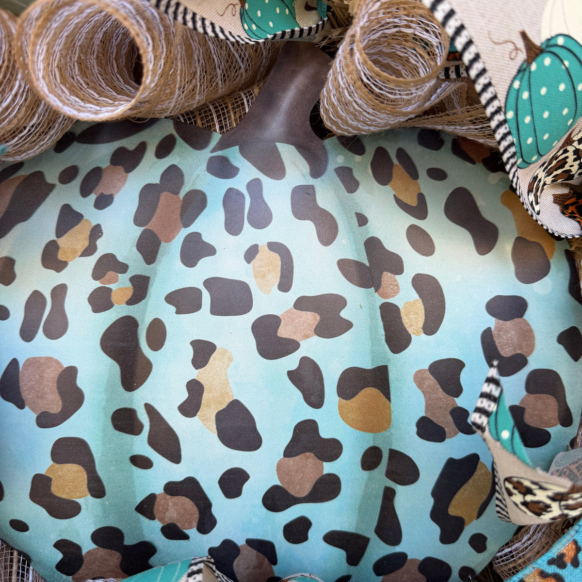 teal leopard-print pumpkin wreath, surrounded by layers of natural-toned deco mesh and coordinating wired ribbons. Pumpkin-print ribbon in teal, orange, cream, and leopard patterns ties the whole design together, while the teal leopard ribbon adds an unexpected pop of color.