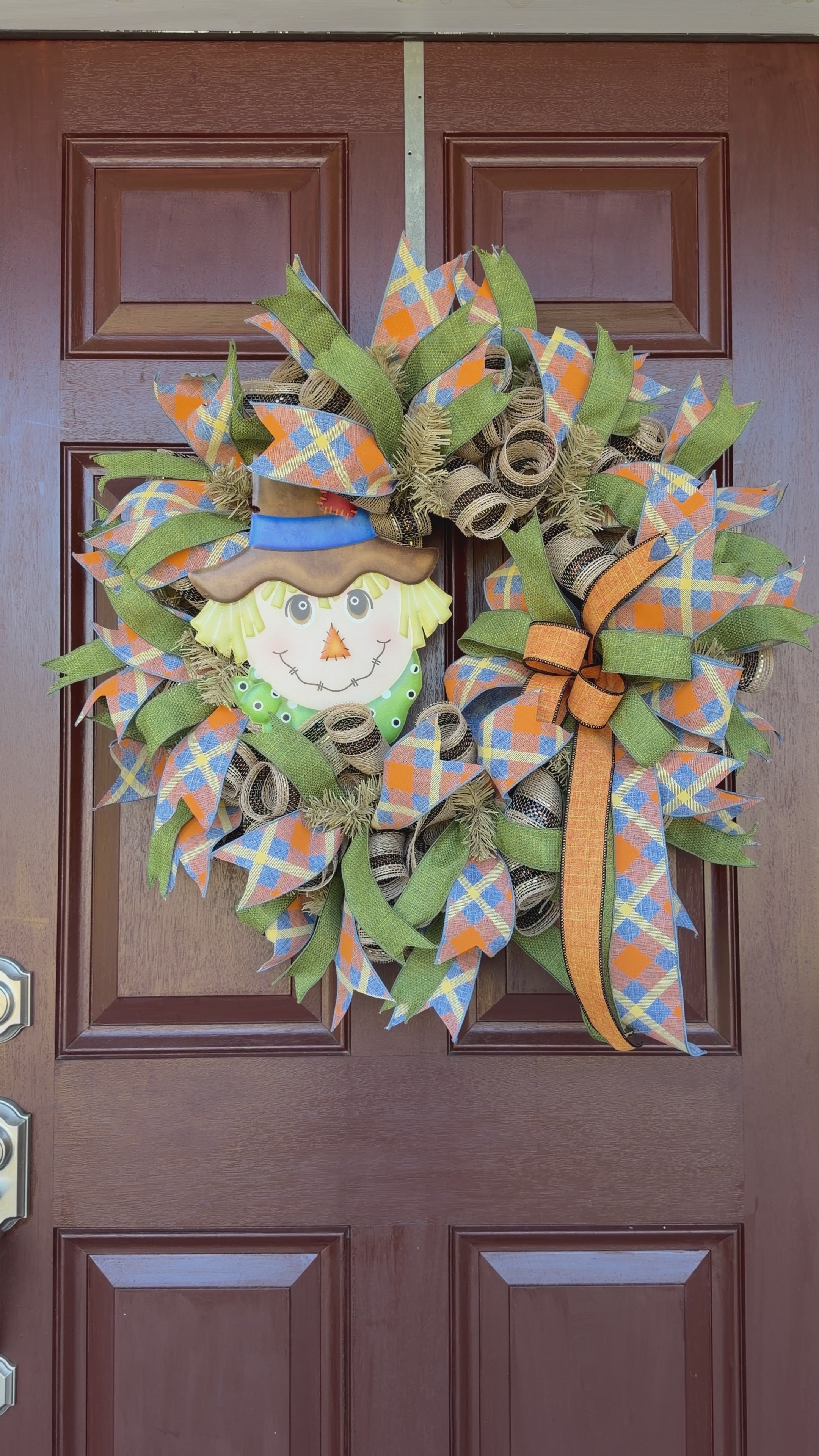colorful scarecrow fall wreath. With its smiling scarecrow, warm autumn tones, and playful plaid ribbon, this wreath feels lighthearted, friendly, and full of seasonal charm.