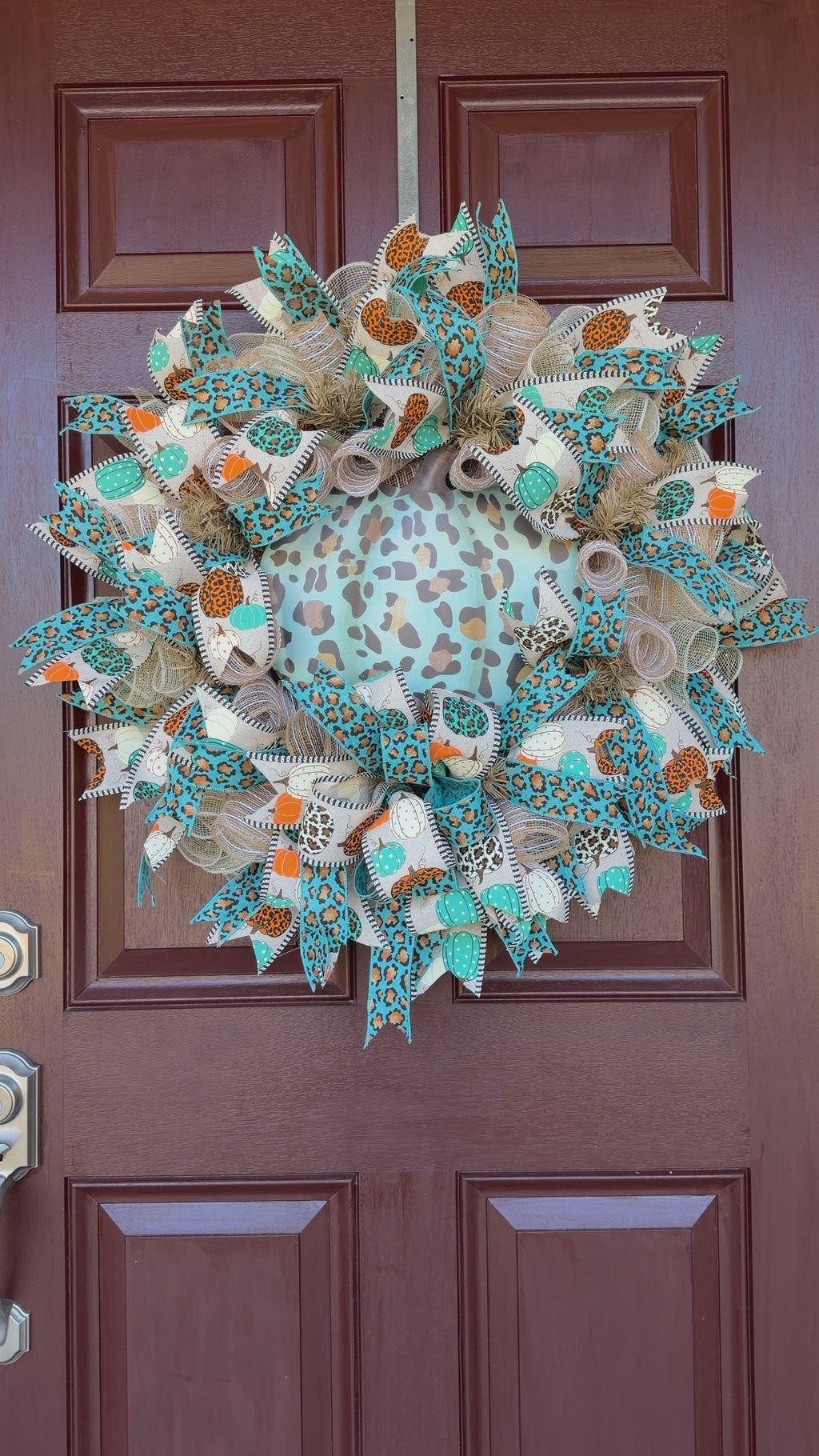 teal leopard-print pumpkin wreath, surrounded by layers of natural-toned deco mesh and coordinating wired ribbons. Pumpkin-print ribbon in teal, orange, cream, and leopard patterns ties the whole design together, while the teal leopard ribbon adds an unexpected pop of color.