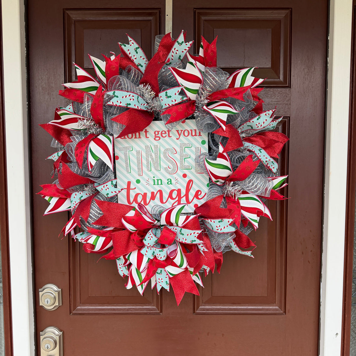 Handmade Christmas deco mesh wreath with silver mesh, red glitter ribbons, candy cane accents, and Don't Get Your Tinsel in a Tangle sign.