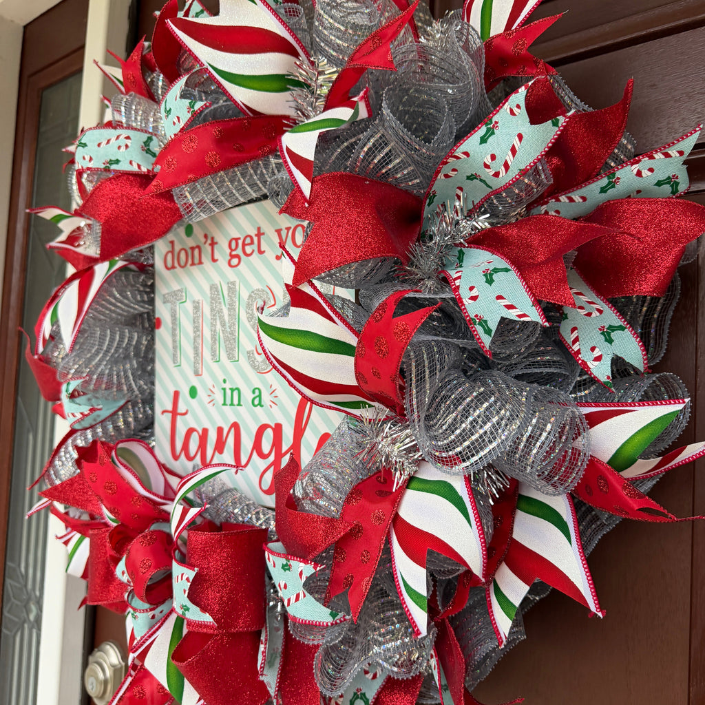 Handmade Christmas deco mesh wreath with silver mesh, red glitter ribbons, candy cane accents, and Don't Get Your Tinsel in a Tangle sign.